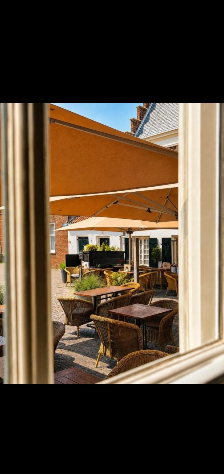 Uitzicht vanuit de Vestigingskamer op het terras met rieten stoelen en parasols